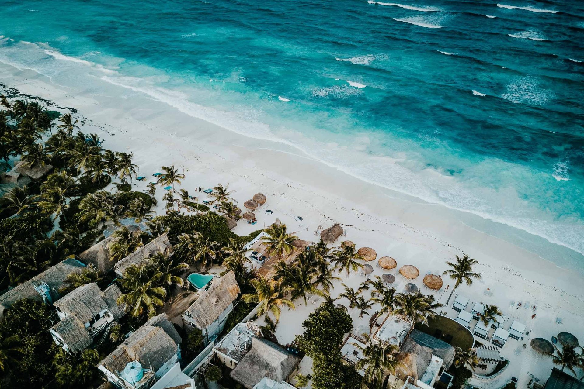 Aerial view of a tropical beach with palm-thatched villas